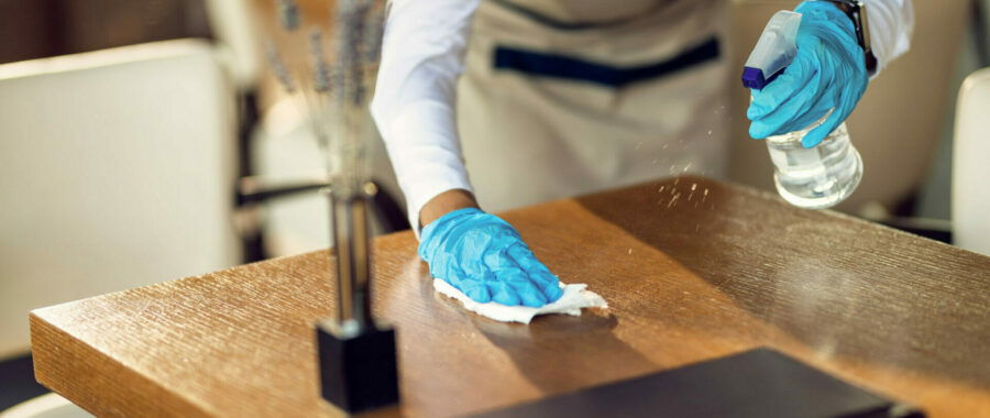 Close-up of waitress wearing protective gloves while cleaning tables with disinfectant in a restaurant.